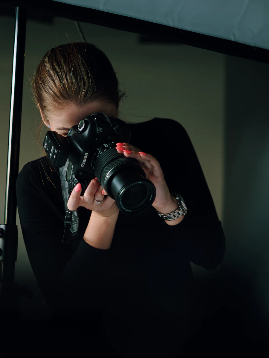 A photographer holding a camera to their eye in low studio light